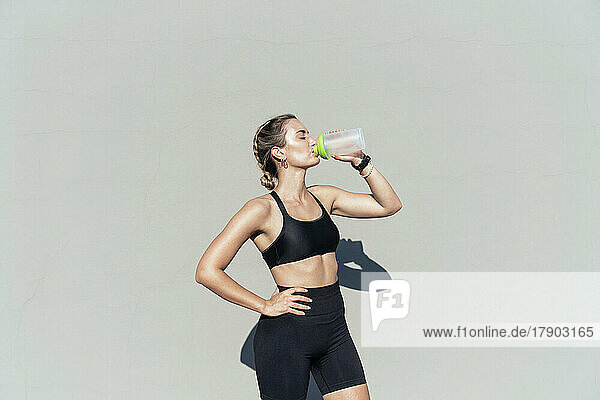 Young athlete with hand on hip drinking water from bottle on sunny day