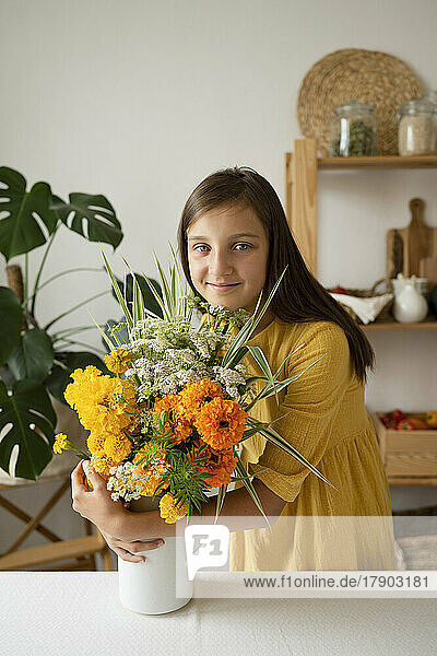Smiling girl hugging flower vase at table in kitchen