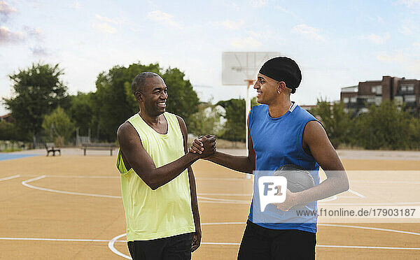 Smiling father and son doing handshake at sports court