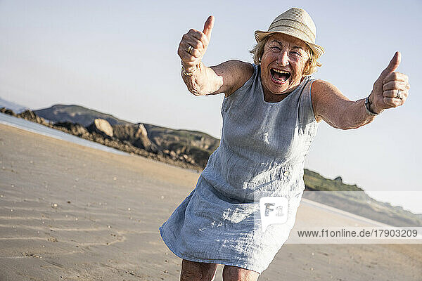 Fröhliche ältere Frau zeigt Daumen nach oben und hat Spaß am Strand