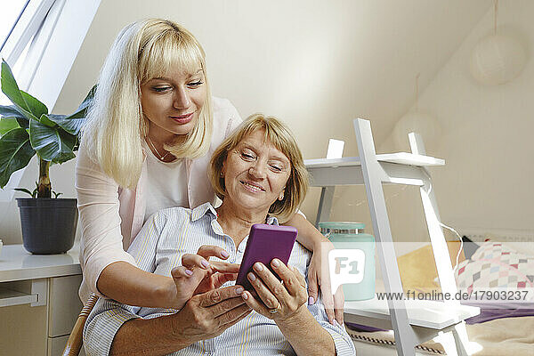 Smiling blond woman teaching smart phone to mother at home