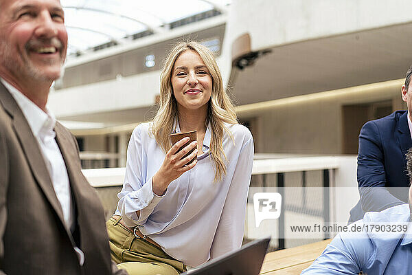 Smiling businesswoman having coffee by colleagues at office