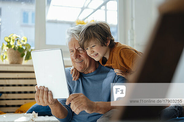 Happy senior man taking selfie with grandson through tablet PC at home