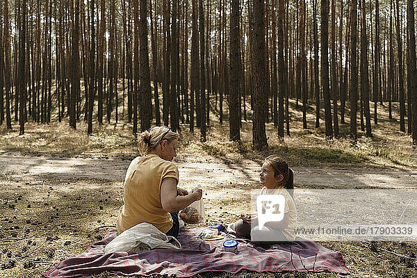 Mature woman and girl enjoying picnic in forest