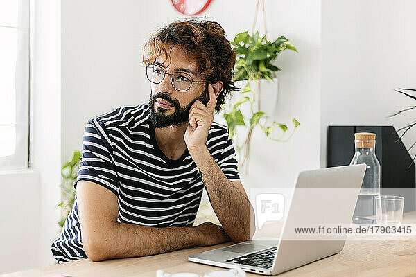 Thoughtful freelancer sitting by laptop at home office