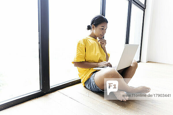 Woman working on laptop leaning against a window