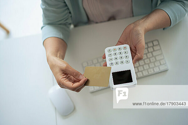 Businesswoman holding credit card and reader at desk in office