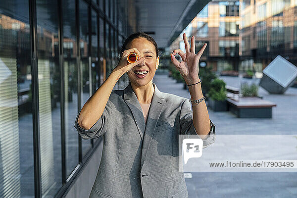 Businesswoman gesturing OK sign looking through rolled paper