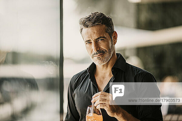 Handsome mature man by glass wall holding drink