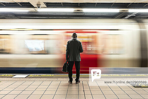 Senior passenger with laptop bag standing in front of speeding train on subway platform