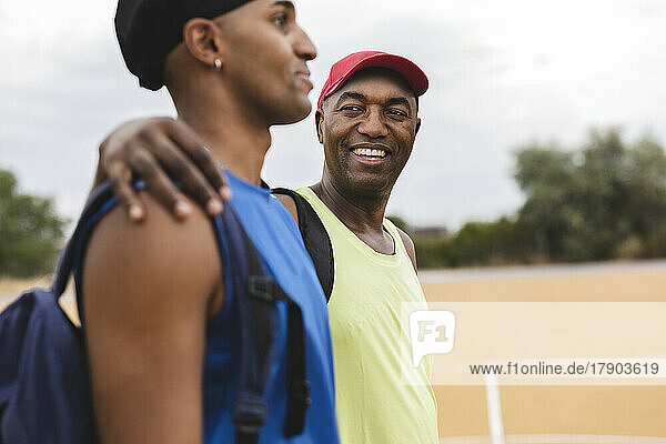 Smiling man with arm around son at basketball court