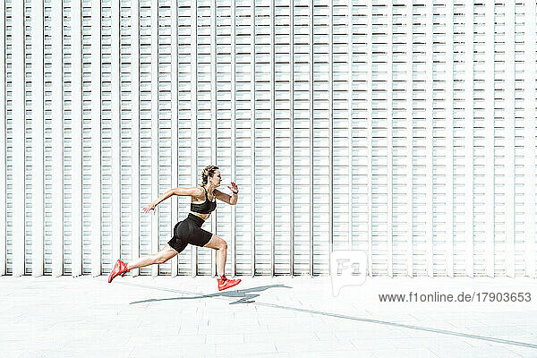 Young athlete running by white wall on sunny day
