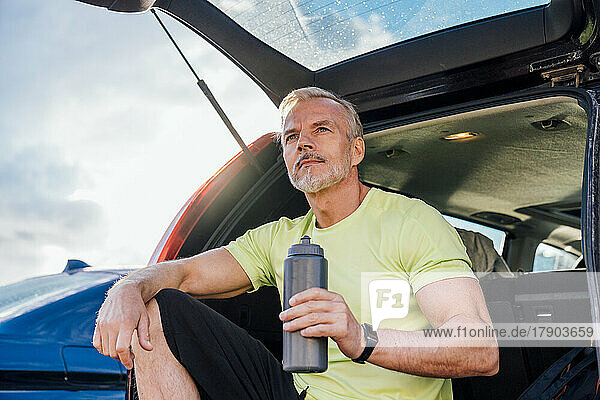 Mature man with bottle sitting in trunk of car