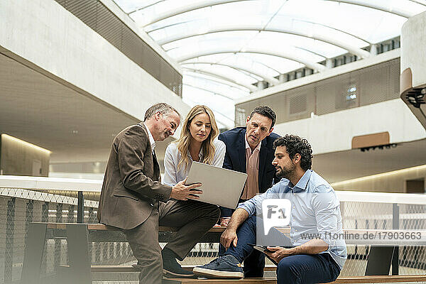 Senior businessman discussing strategy over laptop with colleagues in corridor