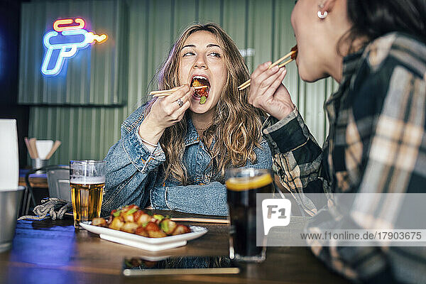 Young lesbian couple eating food with chopsticks at restaurant