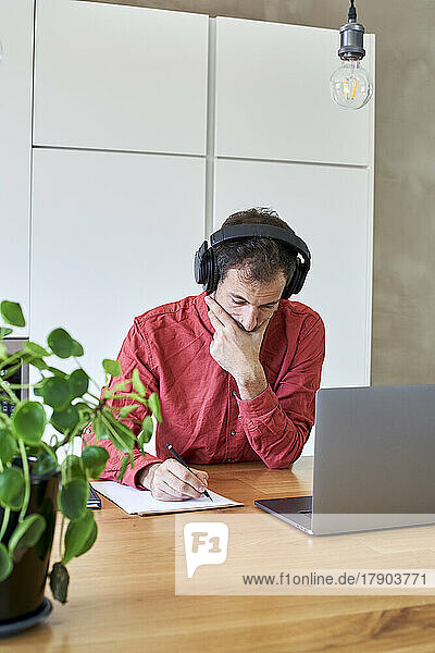 Businessman with wireless headphones writing at home