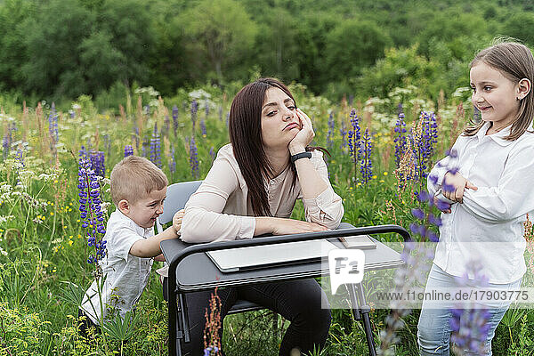 Tired mother with children sitting in meadow