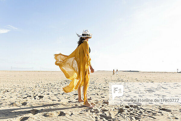Reife Frau mit Hut steht an einem sonnigen Tag am Strand