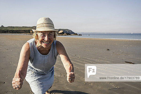 Happy senior woman showing thumbs up at beach on sunny day