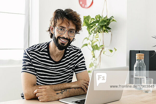 Happy man sitting with laptop at home office