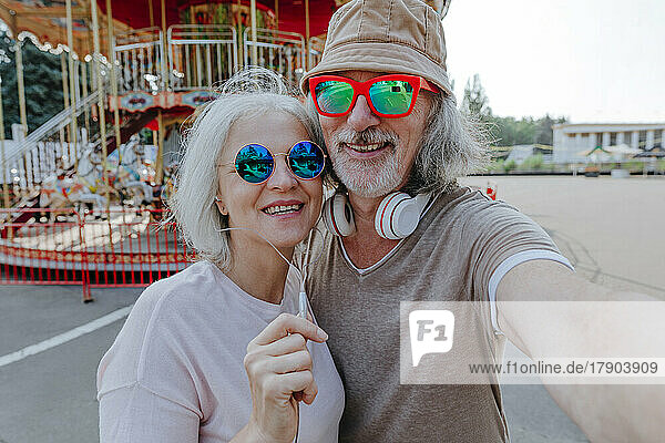 Happy couple wearing sunglasses taking selfie in amusement park