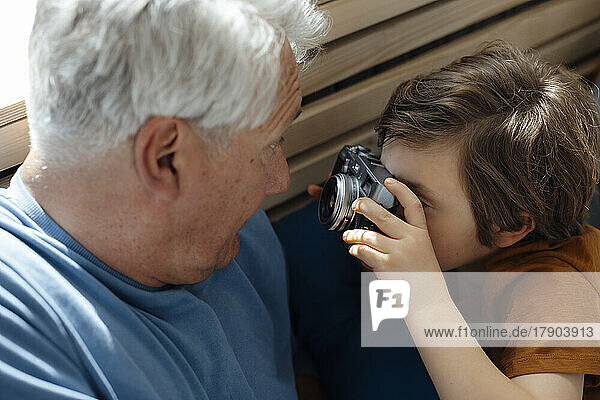 Boy taking picture of grandfather through camera at home