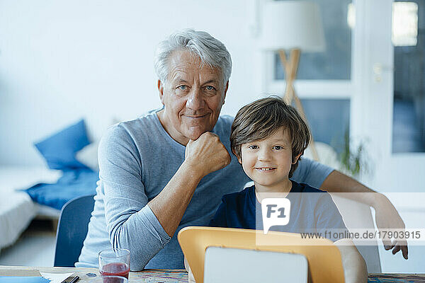 Smiling senior man with hand on chin by grandson at home
