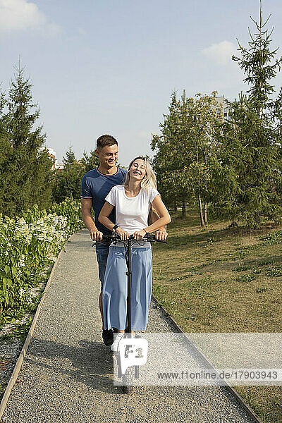 Young woman with boyfriend enjoying electric scooter ride in park
