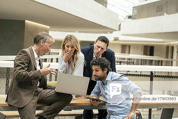 Surprised business colleagues discussing over laptop in corridor