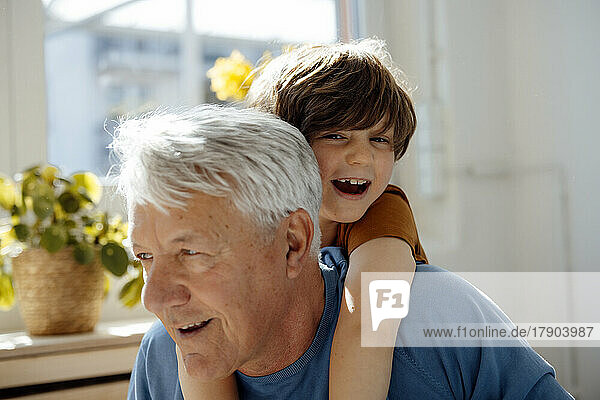 Happy senior man giving piggyback ride to grandson at home