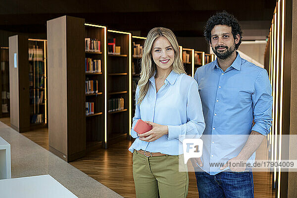 Smiling colleagues standing in illuminated university library