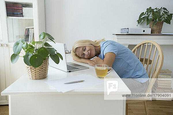 Smiling freelancer with eyes closed relaxing on desk at home office