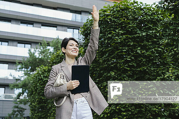 Glückliche Geschäftsfrau winkt mit der Hand  während sie vor dem Gebäude steht