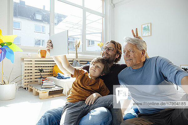Boy taking selfie with father and grandfather through tablet PC at home