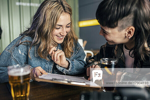 Happy lesbian couple with food menu sitting at table in restaurant