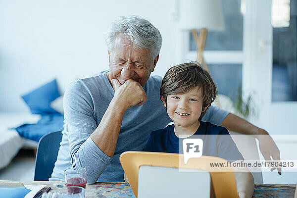 Happy senior man with hand on chin by cute grandson at home
