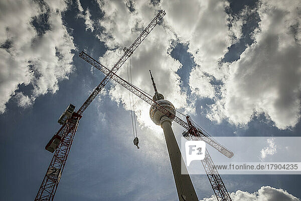 Cranes near Berlin Television Tower under cloudy sky at Alexanderplatz  Berlin  Germany