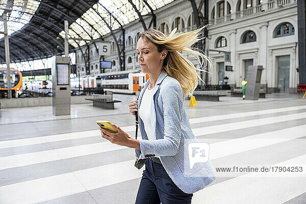 Businesswoman holding smart phone running at railroad station