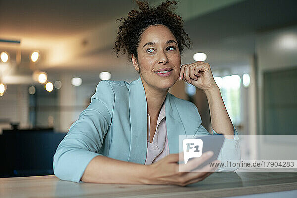 Thoughtful businesswoman with mobile phone at table in office