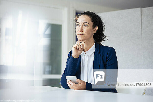 Thoughtful businesswoman holding mobile phone