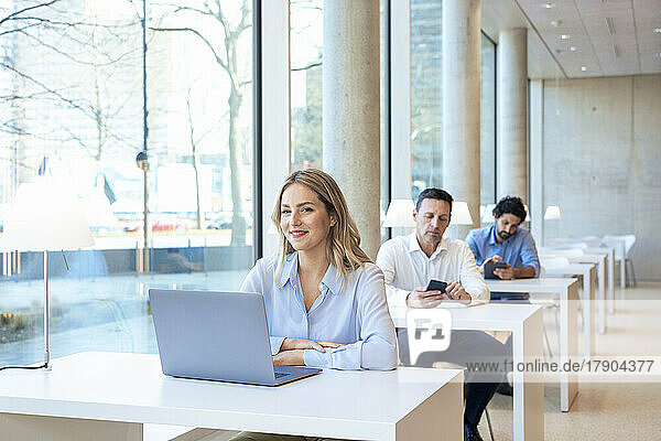 Smiling teacher with laptop on desk in university