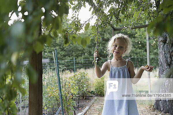 Lächelndes Mädchen hält Pflaumen und Baumstamm im Garten