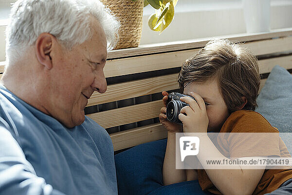 Grandson taking picture of grandfather through camera at home