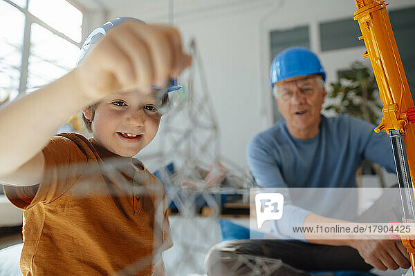 Boy examining electricity pylon model by grandfather at home