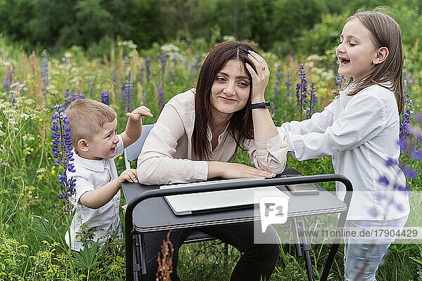 Playful children irritating mother sitting amidst lupine flowers