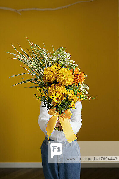 Girl holding bouquet of fresh flowers standing in front of yellow wall at home