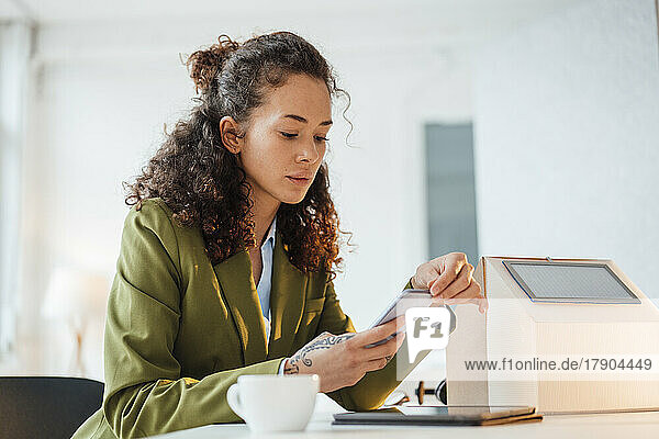 Young businesswoman using smart phone sitting at desk in office