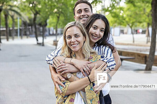 Lächelnder junger Mann umarmt Frauen von hinten im Park