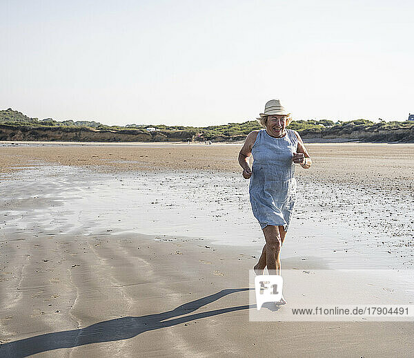 Happy senior woman running at beach on sunny day