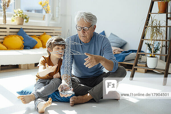 Grandson and grandfather examining electricity pylon model in living room